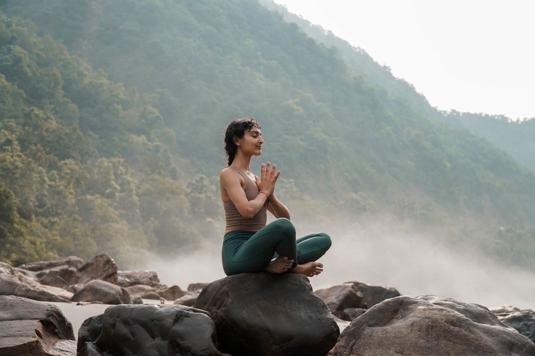 Person sitter i meditation på en klippa vid en dimmig skogflod